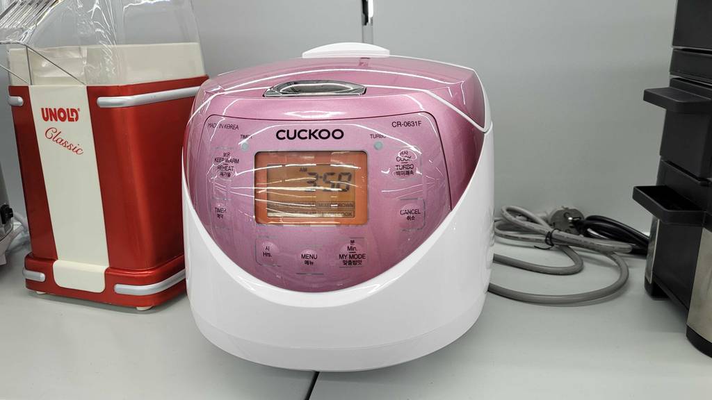 Ein getesteter digitaler-Reiskocher von Cuckoo steht in einem Regal neben anderen Artikeln.