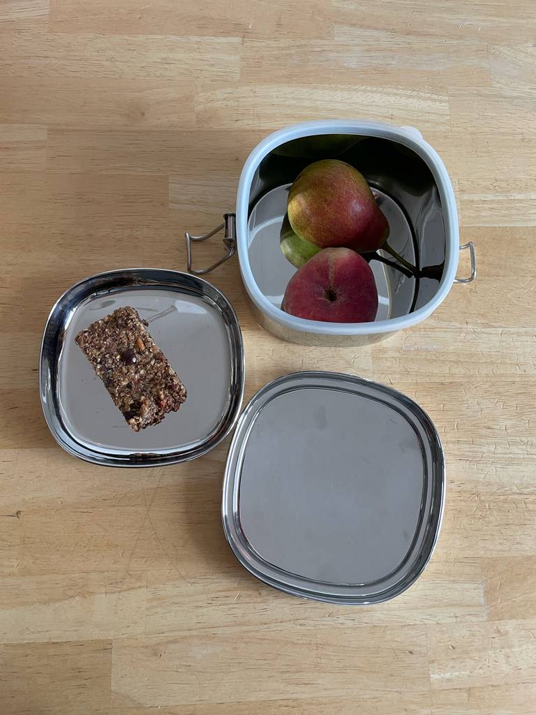 Die geöffnete Metall-Brotdose im Test befindet sich inklusive Obst und Brot auf einem Holztisch.
