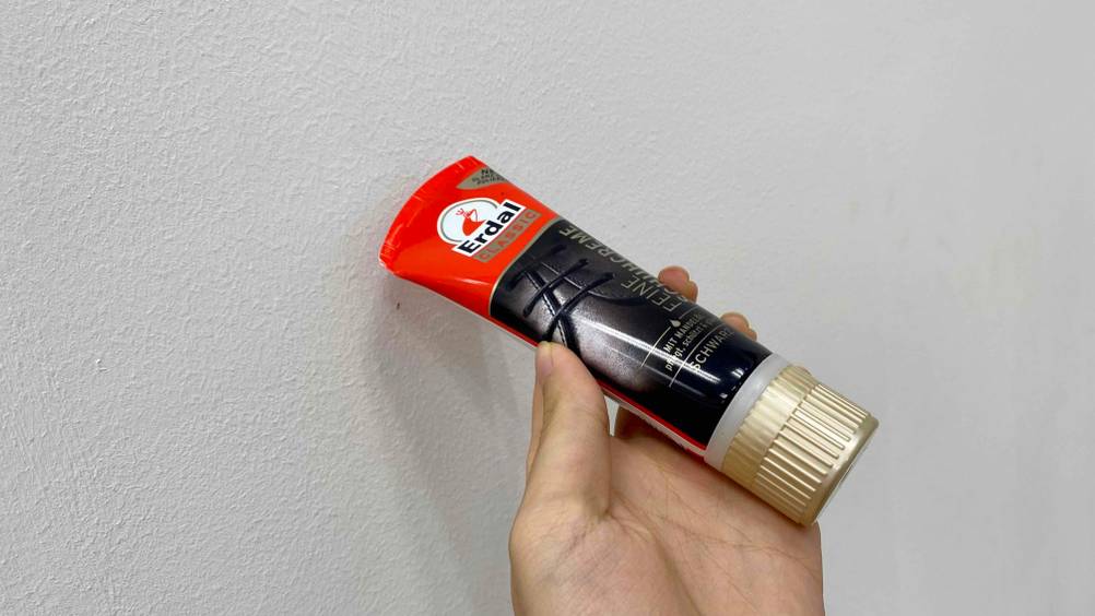 Schuhcreme im Test: Eine Hand hält eine Tube vor einen hellen Hintergrund