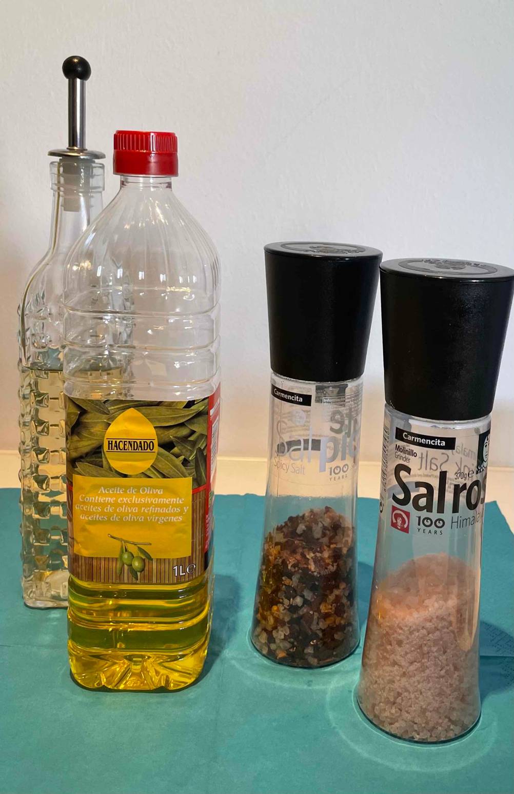 Spanisches-Olivenöl getestet: eine Flasche spanisches-Olivenöl steht neben Gewürzen und dahinter ein Ölbehälter aus Glas ersichtlich.