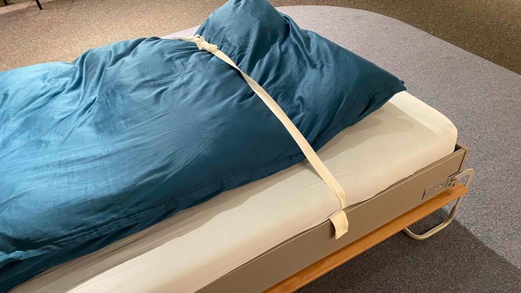 Schrankbett getestet: Das Bett eines Schrankbettes im Fokus, bei welchem eine blaue Bettdecke mit Bändern gesichert ist.