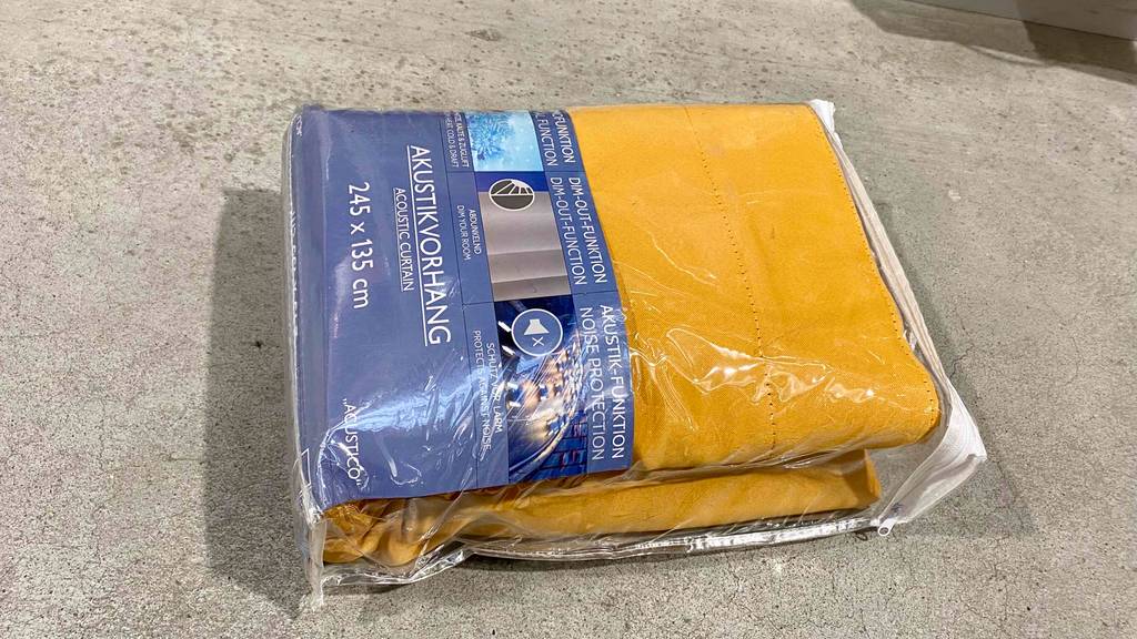 Im Test: Ein verpackter Akustikvorhang liegt horizontal auf einem grauen Boden.