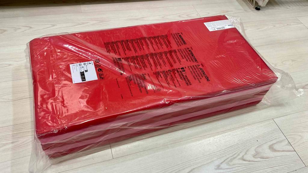 Faltbare-Gymnastikmatte getestet: eine rotfarbene faltbare Gymnastikmatte ist in einem Plastik eingepackt und liegt auf einem Boden.