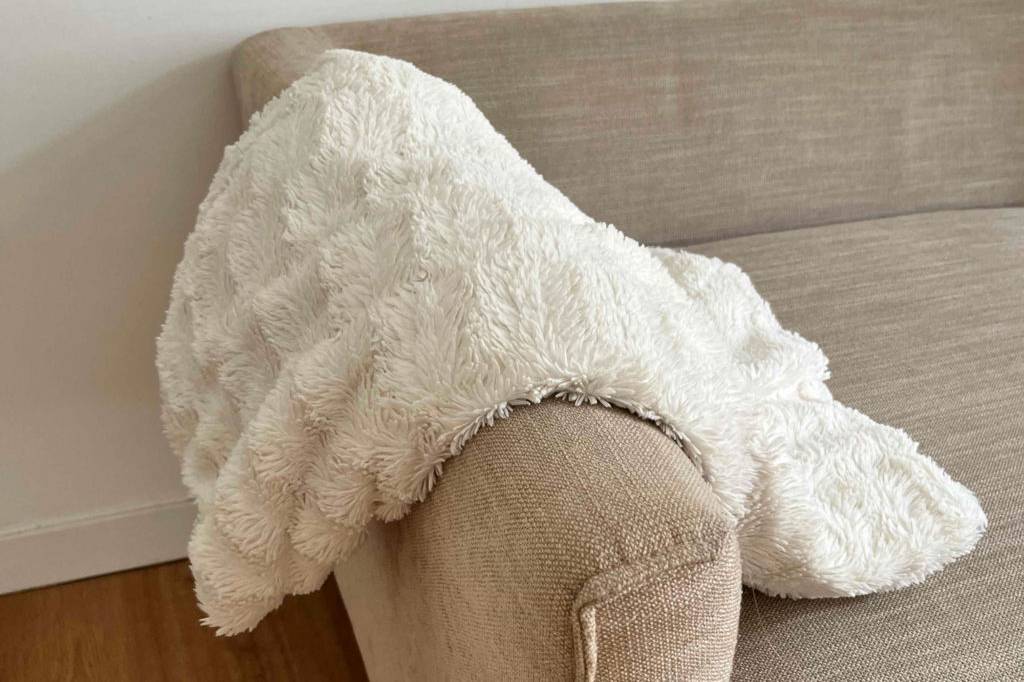 Kuscheldecke im Test: Eine helle Decke liegt über der Lehne eines beigen Sofas
