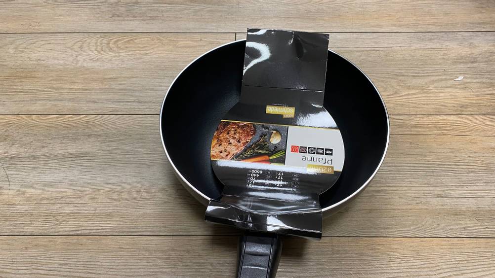 Pfanne-26-cm-Test: schwarze Pfanne mit Papiereinlage darin, worauf man verschiedene Hinweise zum Produkt findet.