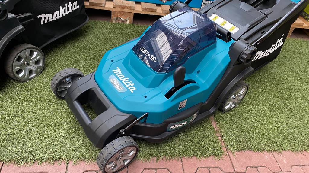 Makita-Akku-Rasenmäher-Test: Makita-Rasenmäher teht mit blauem Vorderteil steht auf Kunstrasen.