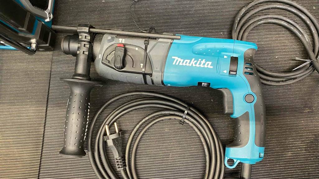 Makita-Bohrhammer im Test: Bohrhammer der Marke Makita liegend auf einer schwarzem Fläche mit schwarzem Kabel ersichtlich.