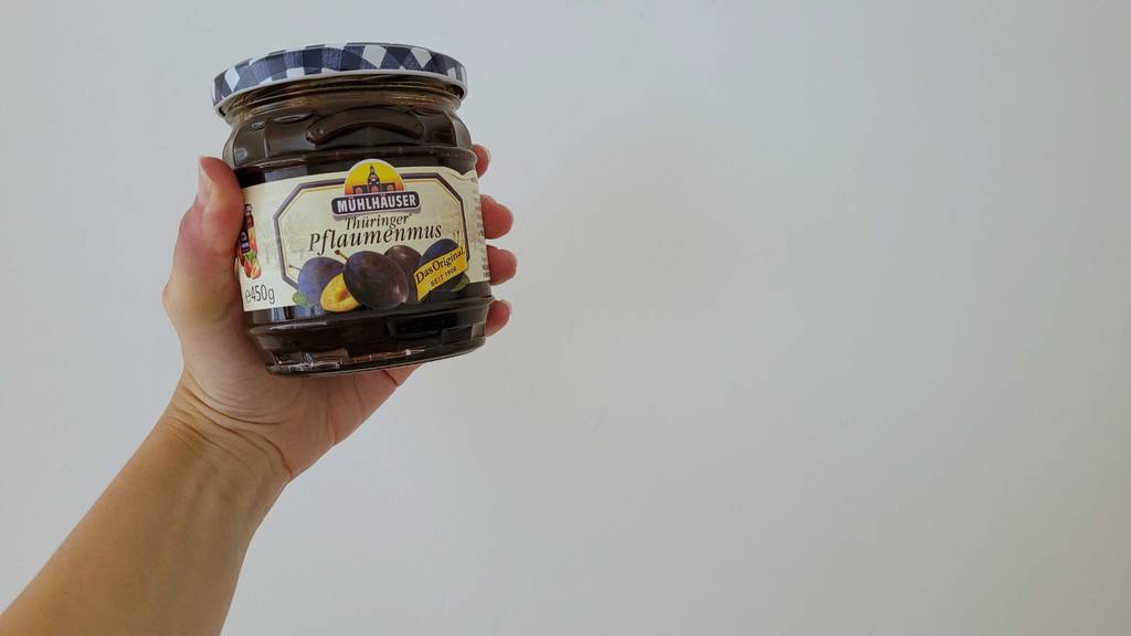 Pflaumenmus im Test: Eine Hand hält ein Glas Mus vor eine helle Wand