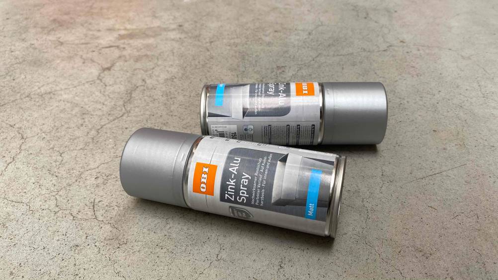 Zinkspray im Test: Zwei Zinksprays von Obi auf einem Boden liegend.