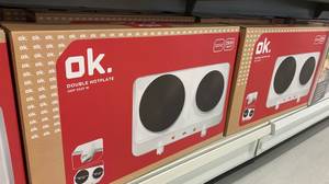 Im Test: Eine verpackte Doppelkochplatte steht neben anderen in einem Regal.