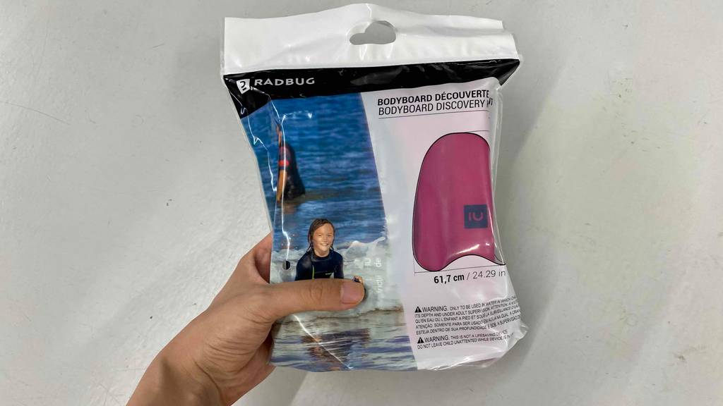 Bodyboard im Test: Eine Hand hält ein noch originalverpacktes Bodyboard vor eine helle Wand