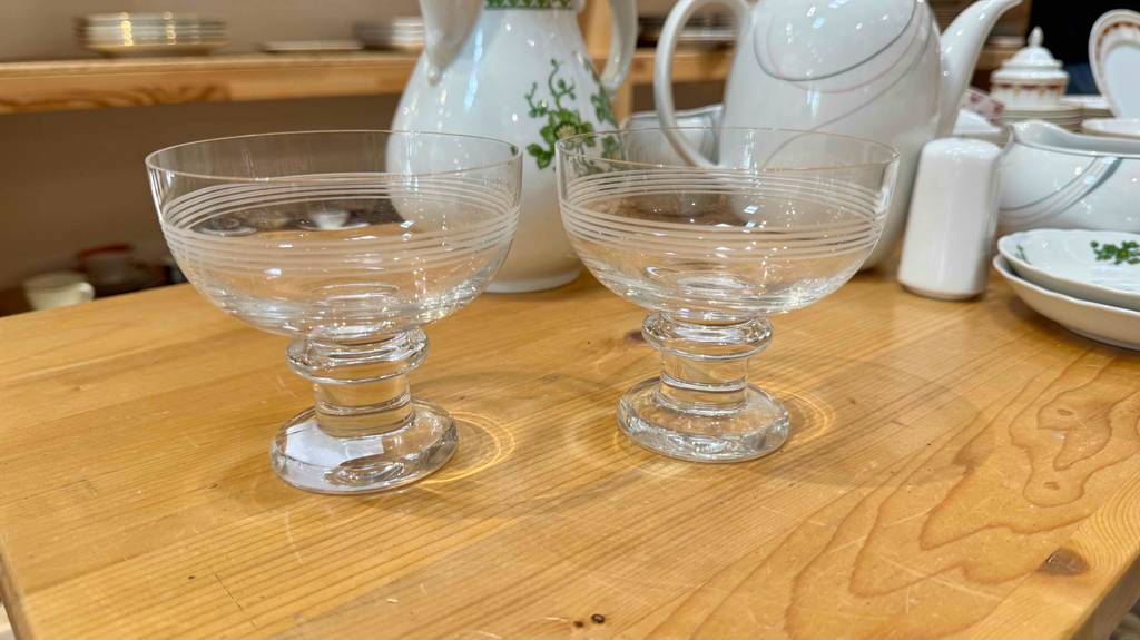 Zwei getestete Eisbecher aus Glas stehen nebeneinander vor einem Kaffeeservice im Verkauf.