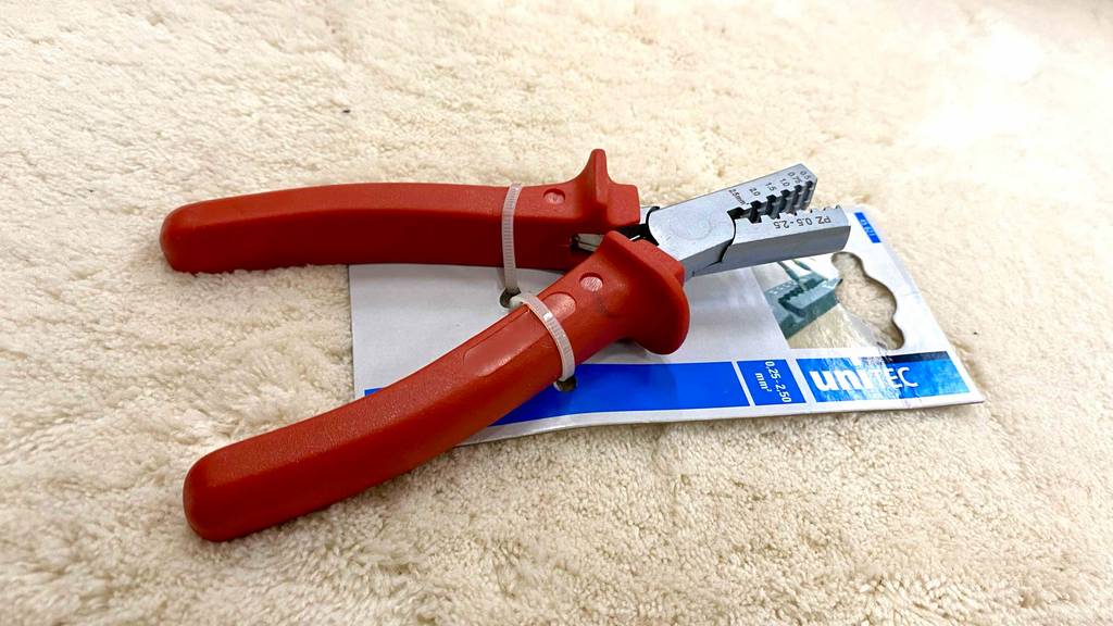 Aderendhülsenzange-Test: eine Aderendhülsenzange ist mit Kabelbindern an die Verpackung befestigt, welche auf einem beigefarbenen Teppich liegt.