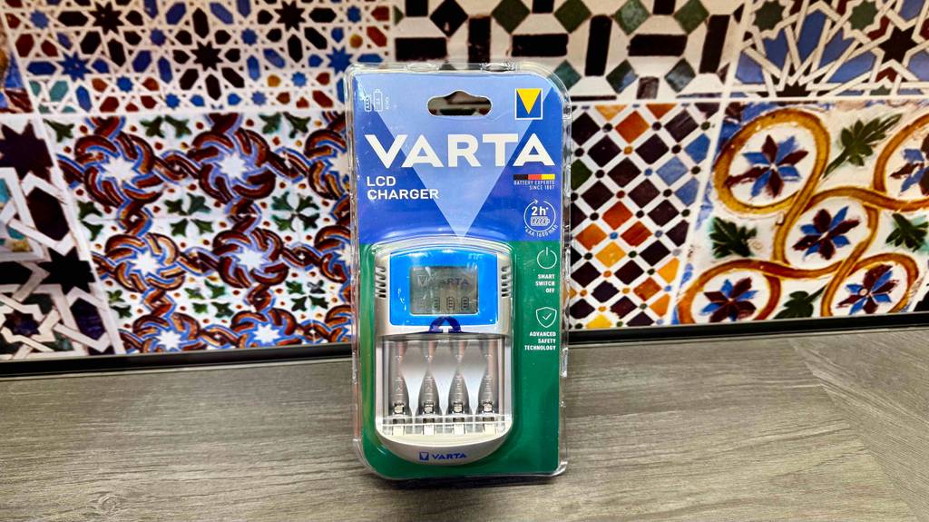 Das Varta-Ladegerät im Test steht in der transparenten Verpackung vor einem bunten Fliesenbelag.