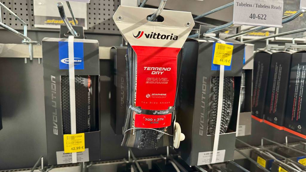 An einem Verkaufsregal hängen die roten Verpackungen mit dem Faltreifen im Test neben weiteren Reifentypen.