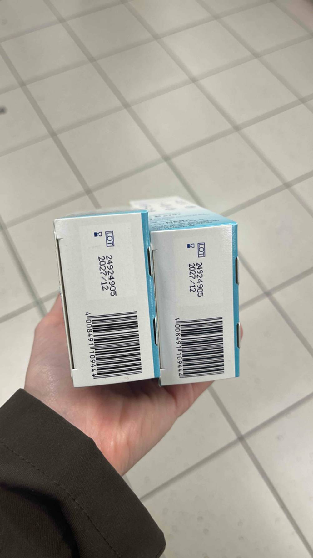 Die Unterseiten der Verpackungen des getesteten Warzenvereisers sind im Fokus, während das Ablaufdatum ersichtlich ist.