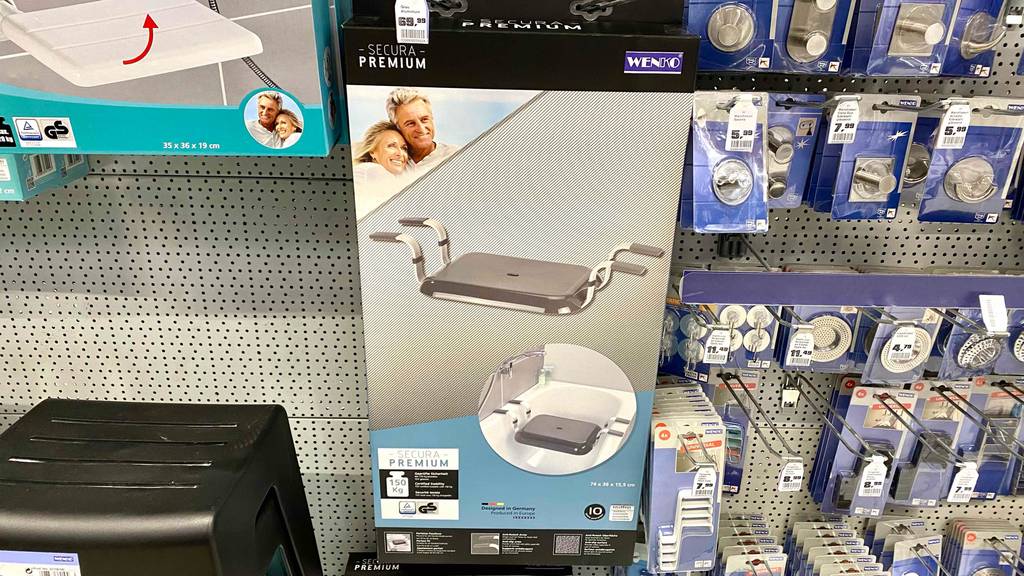 Ein getesteter Badewannensitz in Verpackung hängt neben anderen Produkten im Regal.