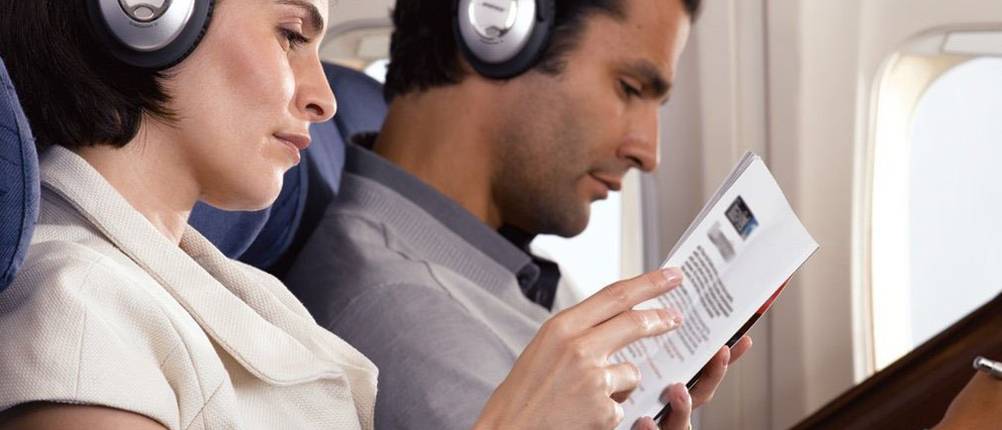 Noise-Cancelling-Kopfhörer-Test: Mann und Frau mit Kopfhörern in einem Flugzeug sitzend