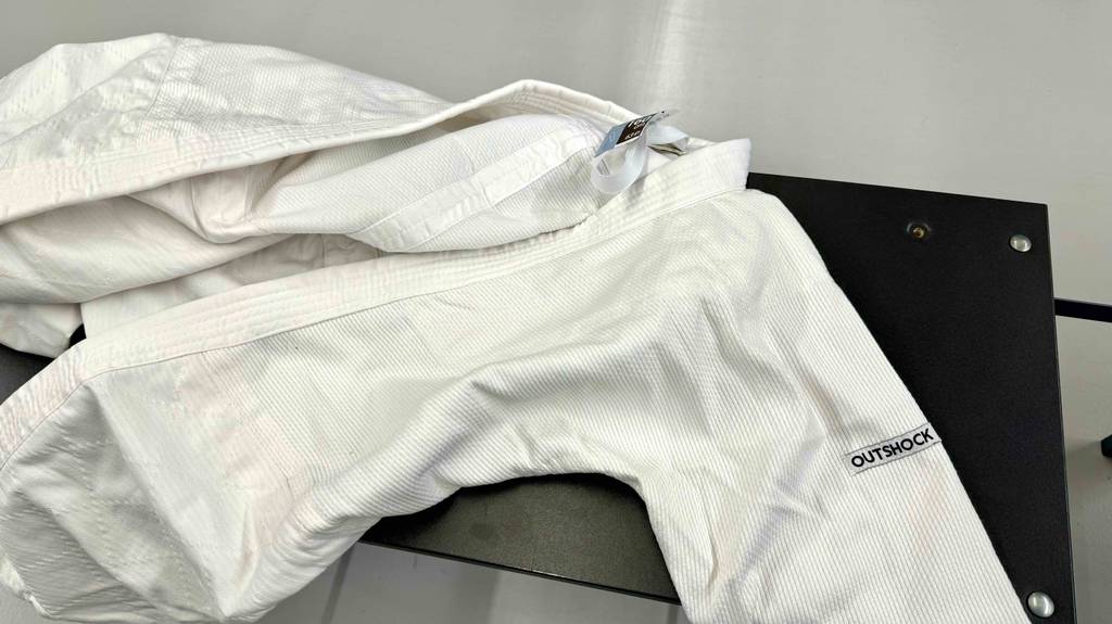 Getestet:Auseinander gefalteter Judoanzug in der Farbe Weiß liegt auf einer schwarzen Sitzbank.