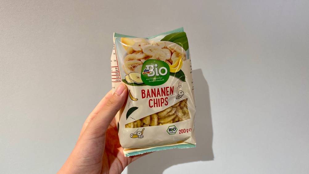 Bananenchips getestet: Eine Hand hält eine Packung vor eine helle Wand.