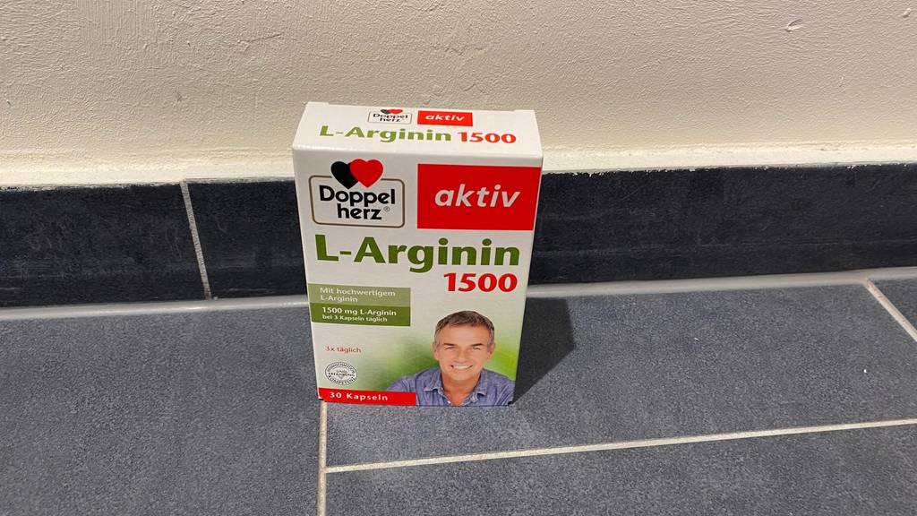 Auf einem grauen Fließenboden steht eine Packung des getesteten L-Arginins