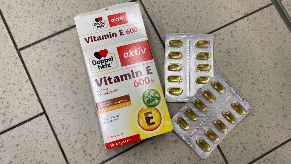 Eine Packung des getesteten Vitamin E und zwei Tablettenblister auf einem Fließenboden.