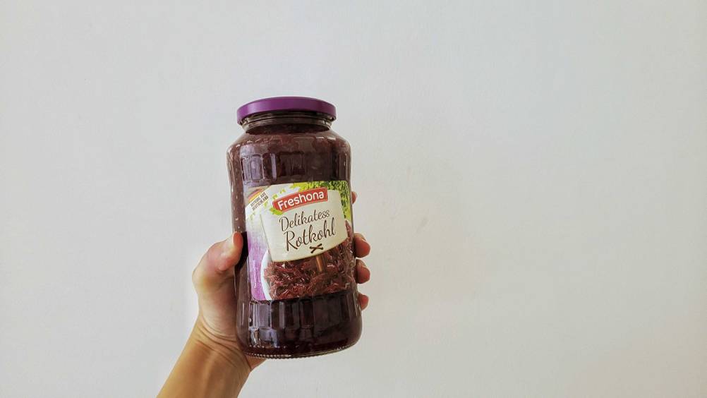 Rotkohl im Test: Eine Hand hält ein Glas Rotkohl vor eine helle Wand