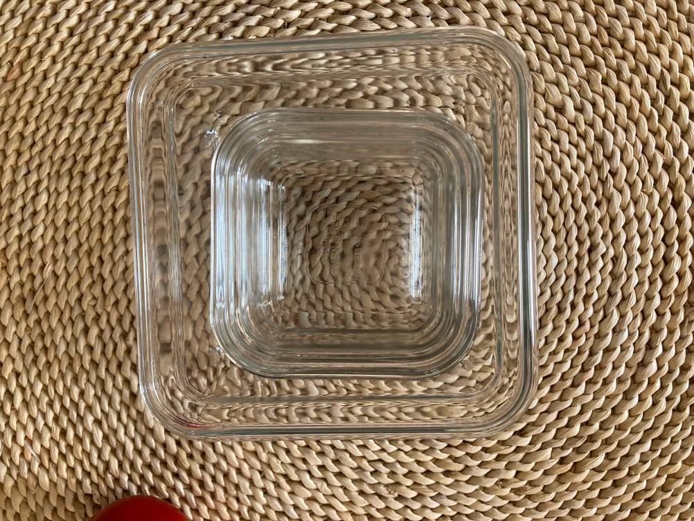Zwei unterschiedlich große Frischhaltedosen aus Glas stehen ineinander auf einer beigen Fläche.