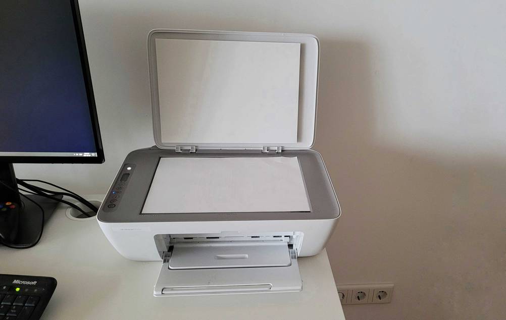 Hp-Multifunktionsdrucker getestet: ein Hp-Multifunktionsdrucker mit geöffnetem Scannerdeckel steht neben einem Bildschirm.