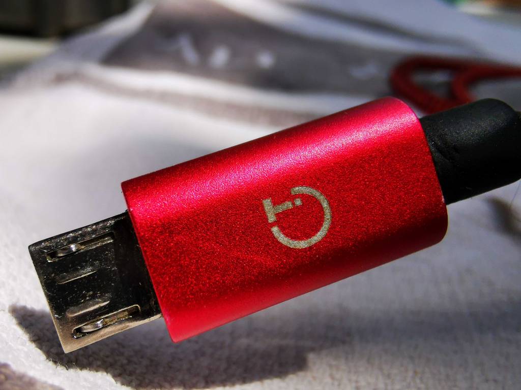 Das Micro-USB-Kabel im Test liegt, mit Fokus auf dem roten Stecker inklusive Markenzeichen auf einer weißen Oberfläche.