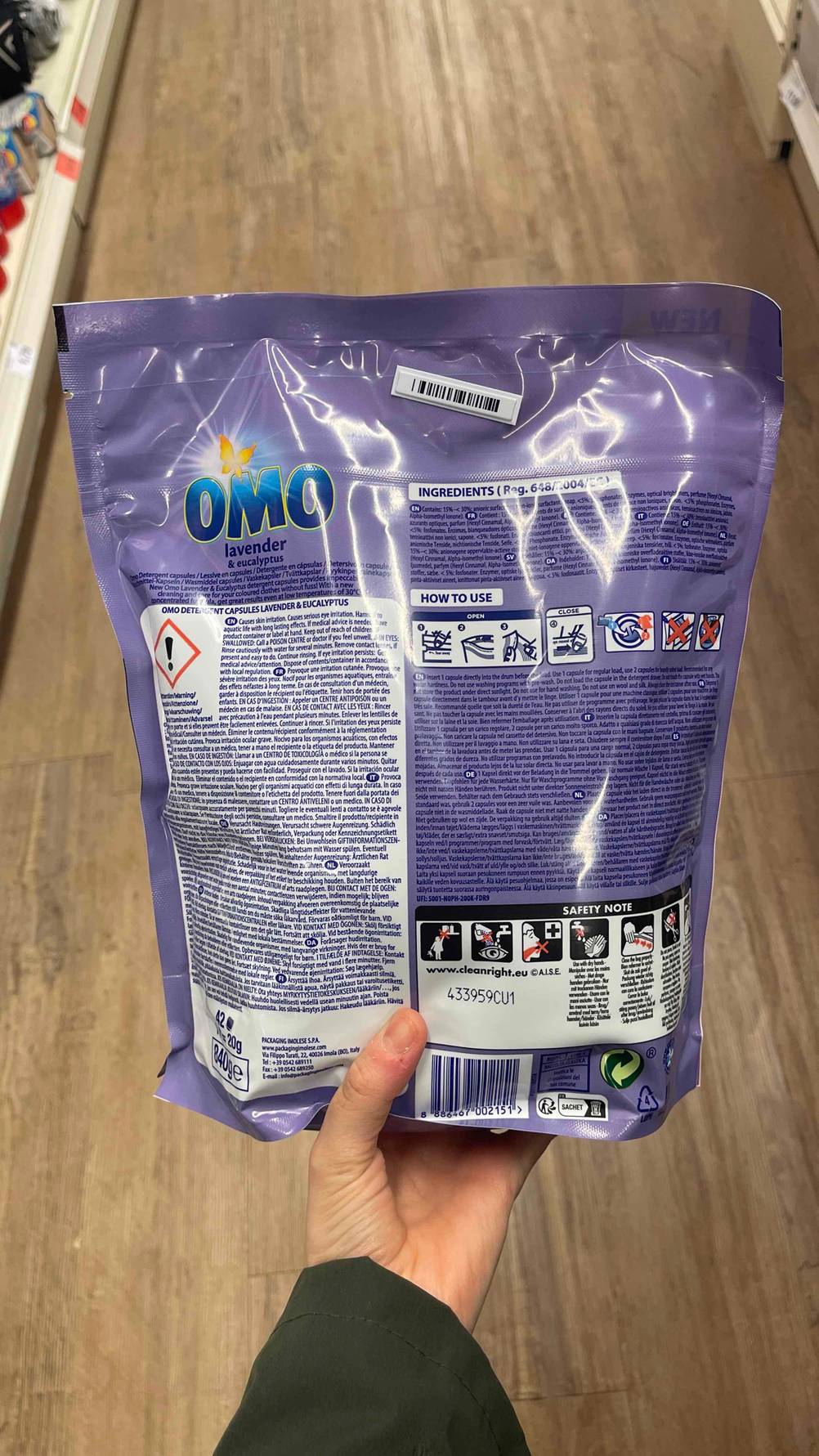 Die Verpackungsrückseite des getesteten Omo-Waschmittel in der Farbe Lila wird in der Hand gehalten.