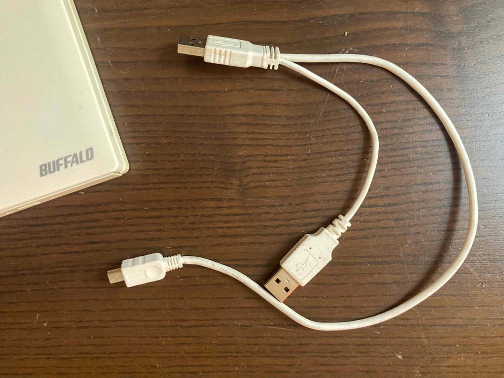 Neben der Ecke eines getesteten Externen DVD-Laufwerks liegen Kabel auf einer Holzfläche.