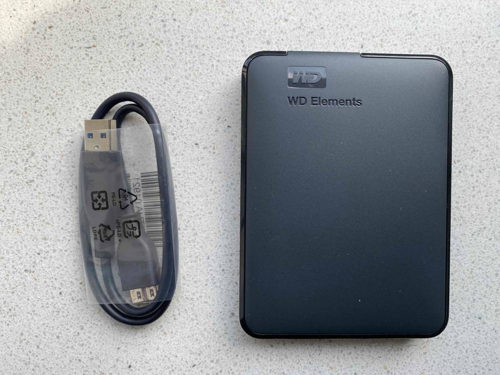 Externe Festplatte von WD im Test auf einem grauen Untergrund, daneben ein Kabel.