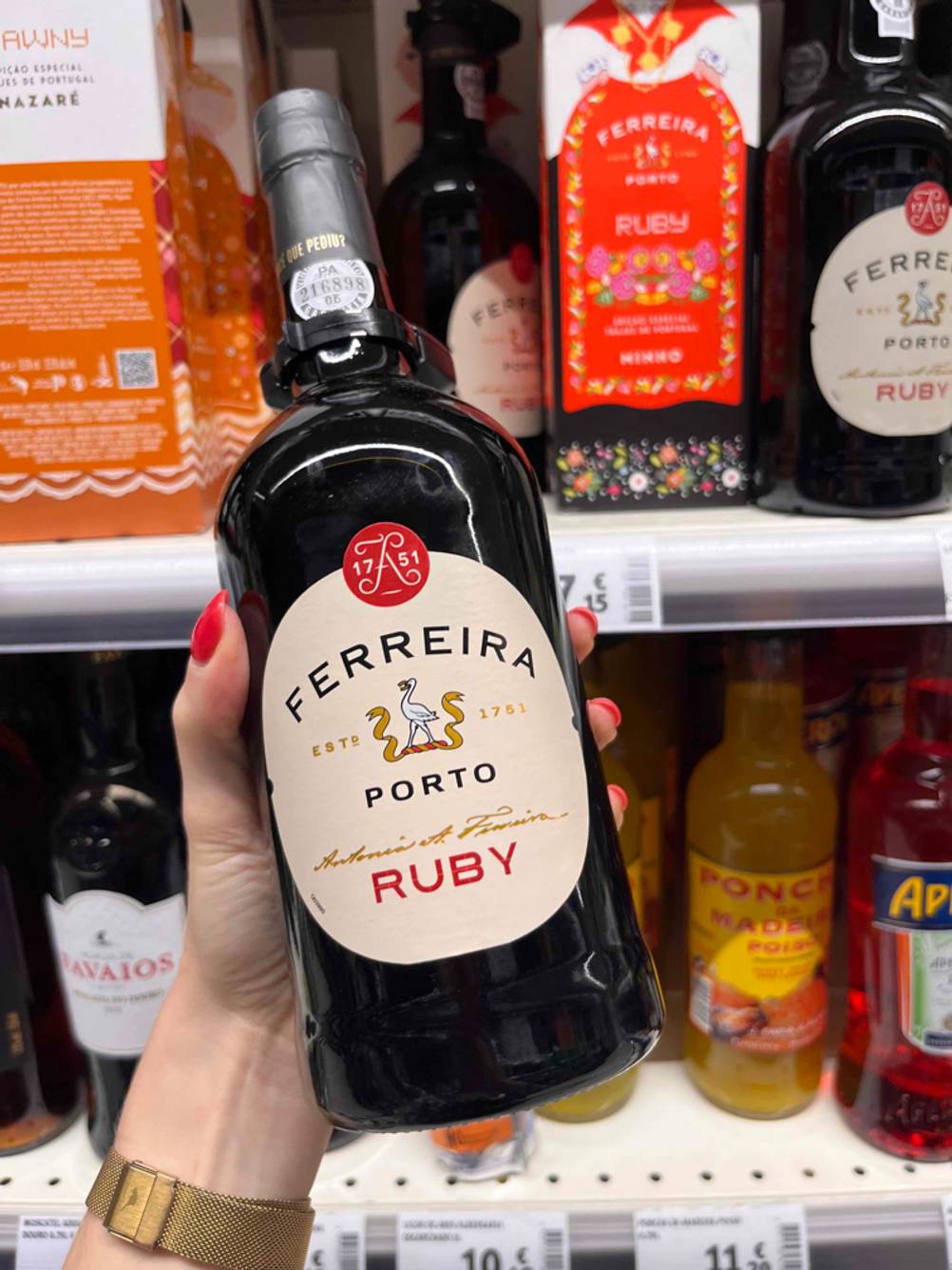 Eine Hand hält eine getestete Flasche Portwein vor ein Verkaufsregal.