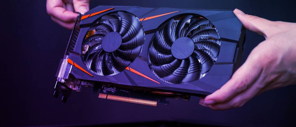 8GB-Grafikkarten-Test: Eine Person hält eine Grafikkarte über einen Computer.