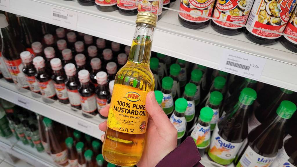 Ein getestetes Senföl wird vor einem Regal in der Hand gehalten.