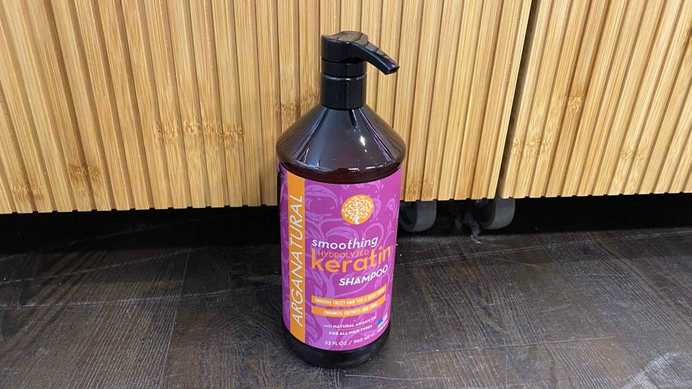 Eine Flasche getestetes Keratin-Shampoo auf einem dunklen Boden vor einer Holzwand.