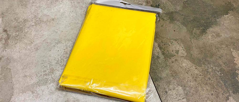 Regenponcho getestet: ein gelber Regenponcho in Plastikverpackung auf einem Boden platziert.