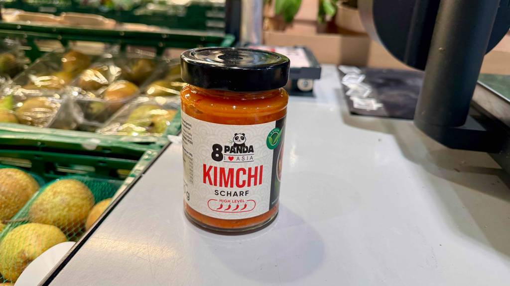 Ein Glas mit Schraubverschluss, in dem sich getesteter Kimchi befindet, steht im Geschäft bei den frischen Früchten.