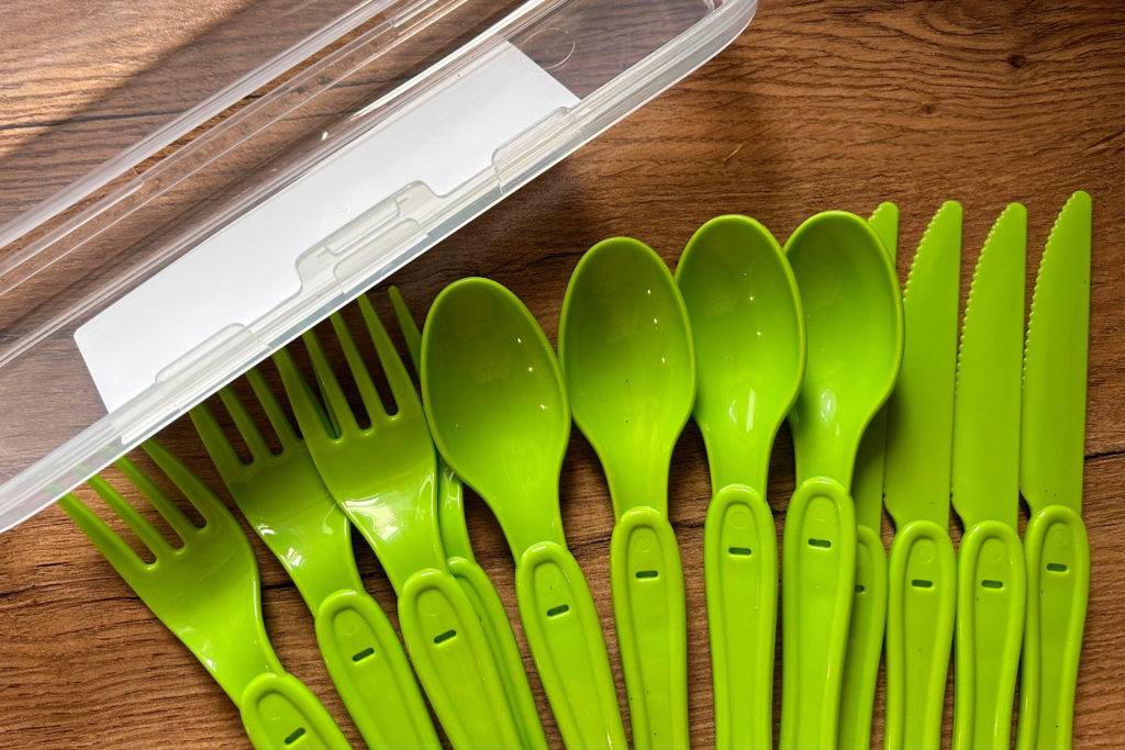 Grünes Campingbesteck bestehend aus Löffeln, Gabeln und Messer - neben einer geöffneten Plastikbox.