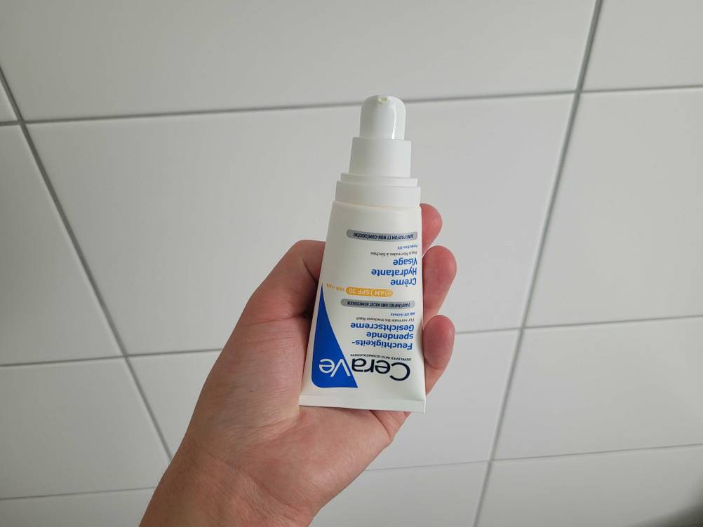 Tagescreme mit LSF getestet: Eine Hand hält eine Tube vor eine Fließenwand.