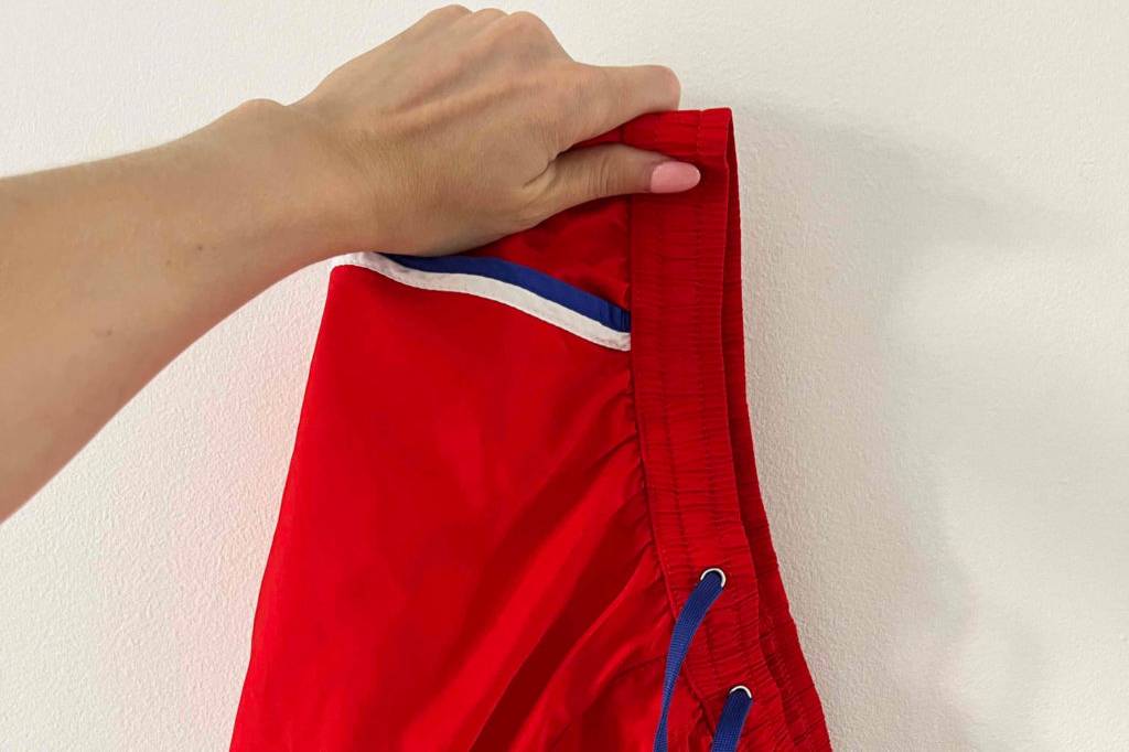 Badehose getestet: Eine Hand hält eine rote Badehose vor eine helle Wand