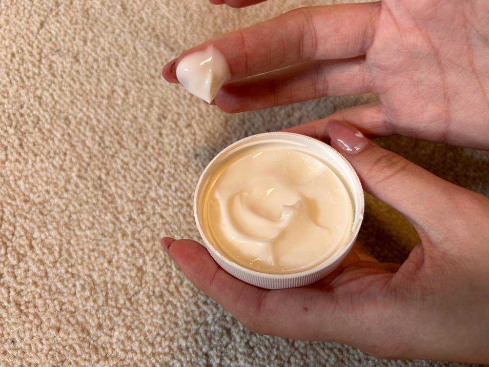 Ein Finger mit der Schrundensalbe im Test neben einem Deckel mit Creme.