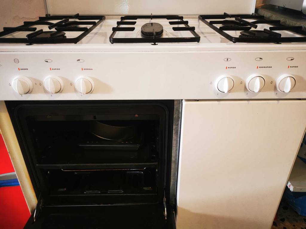 Vorderansicht auf das getestete 5-flammige Gaskochfeld, das sich auf einem weißen Küchenherd mit geöffnetem Backofen befindet.