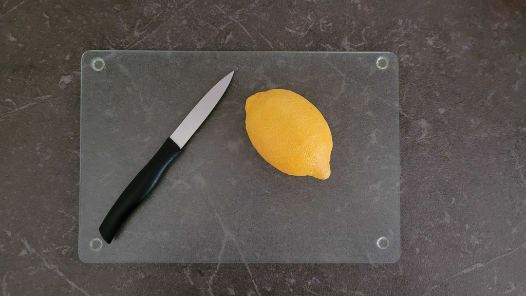 Schneidebrett aus Glas mit einer Zitrone und Messer darauf.