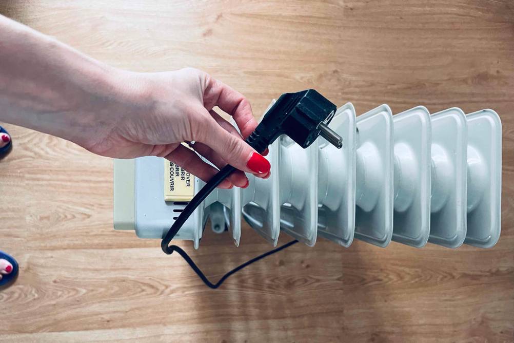 Getestete Heizung: Stehender elektrischer Heizkörper von oben, mit Frauenhand, die das Stromkabel festhält.