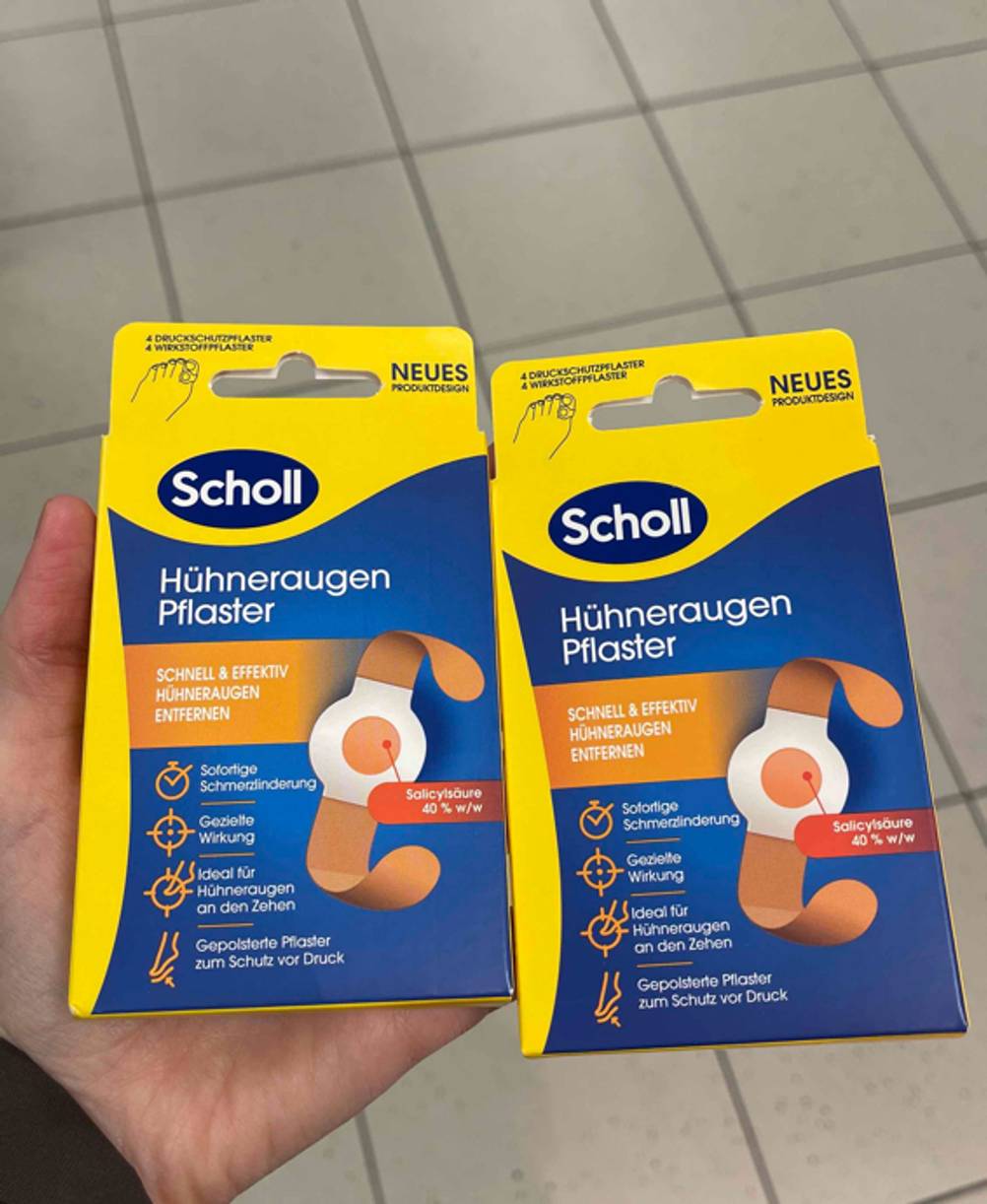 Die zwei identischen Verpackungen der getesteten Hühneraugenpflaster von Scholl werden in der Hand gehalten.