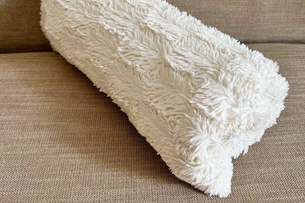 Kuscheldecke im Test: Eine Decke liegt zusammengerollt auf einem beigen Polster