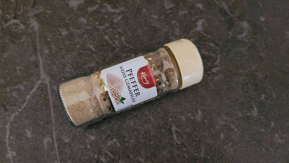 Weißer Pfeffer getestet: Ein Glas Pfeffer liegt quer auf einer dunklen Oberfläche