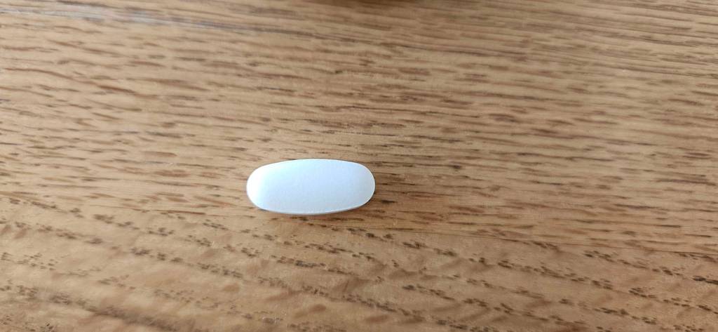 Im Test: Eine Tablette Lysin auf einer Holzfläche liegend.